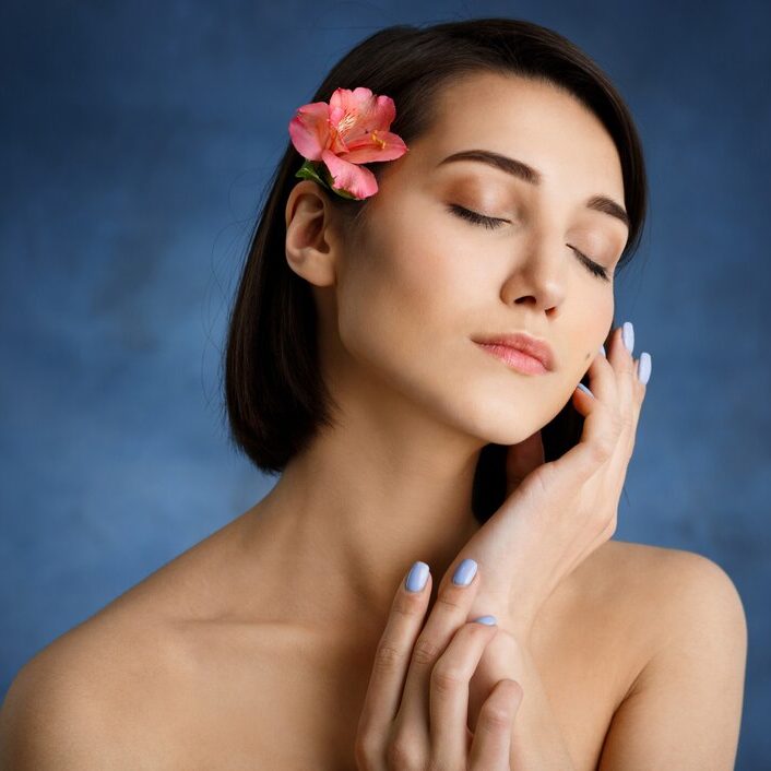 close-up-portrait-tender-young-woman-with-pink-flower-hair-blue-wall_176420-2717
